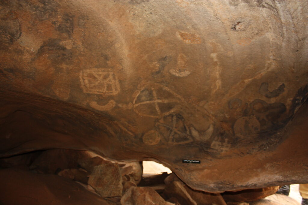 A photograph shows a cave with assorted etchings of lines, circles, and squares drawn across the ceiling.