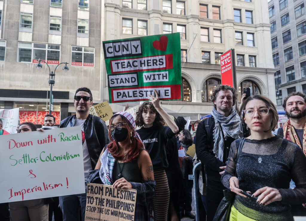 Several people stand in front of a large stone building holding posters with phrases including CUNY Teachers Stand With Palestine, Down with racial settler-colonialism and imperialism, and from Palestine to the Philippines, stop the US war machine.