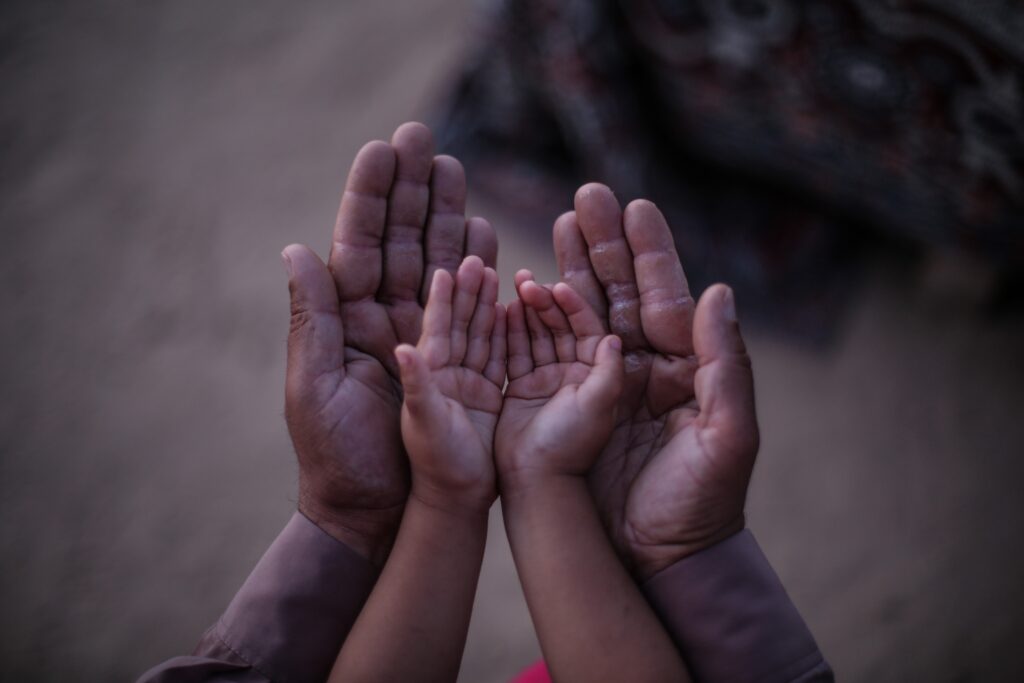 Reaching forward, an adult pair of hands cup those of a child.