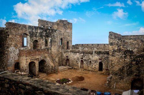 The ruins of a gray stone building stand below a cerulean sky with fluffy white clouds.