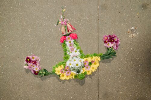 Green, purple, red, yellow, and white flowers arranged in the shape of a uterus lie on a sunlit sidewalk.