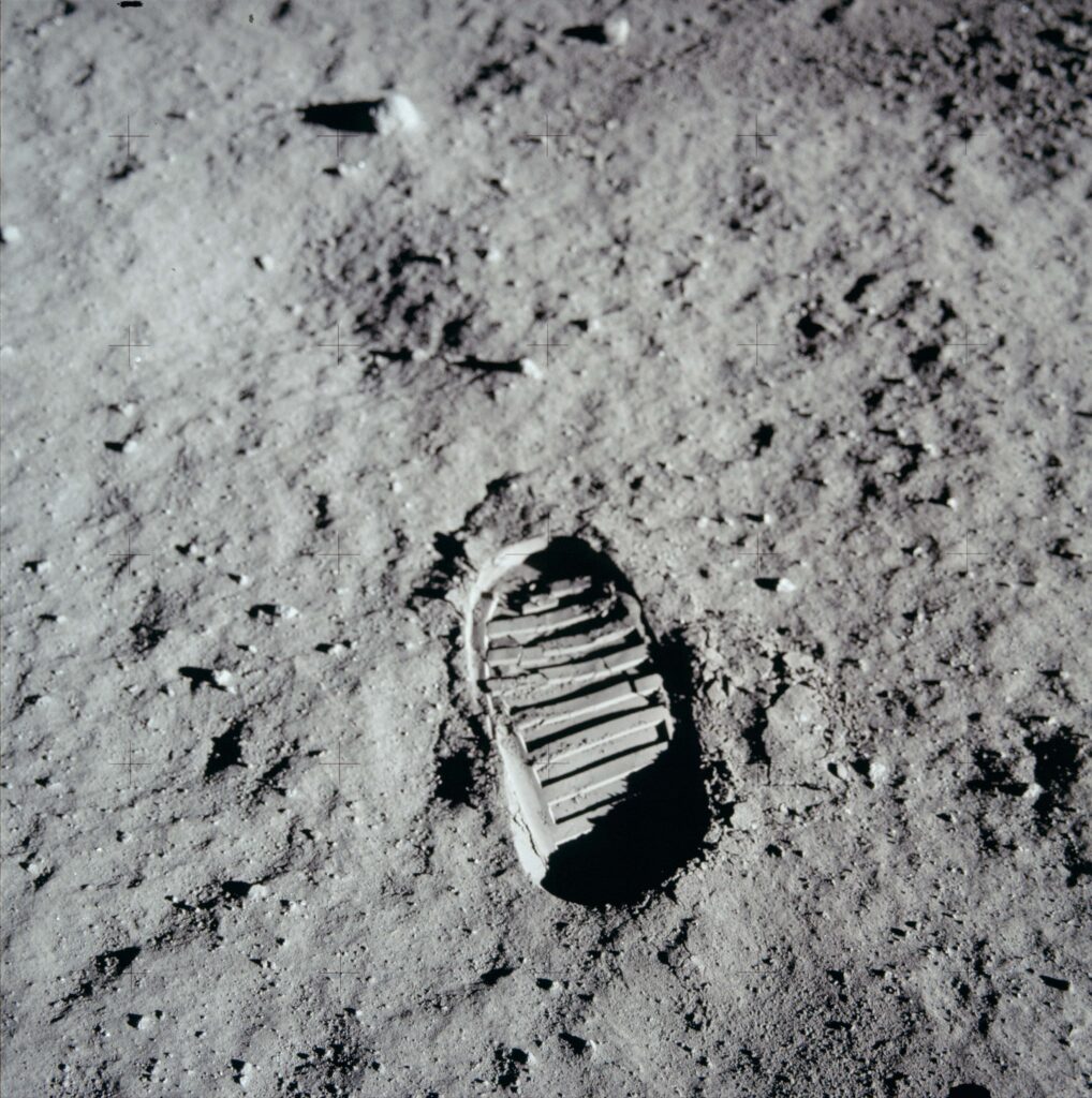 A single boot print makes a distinct impression on a gray surface of dust and rocks.